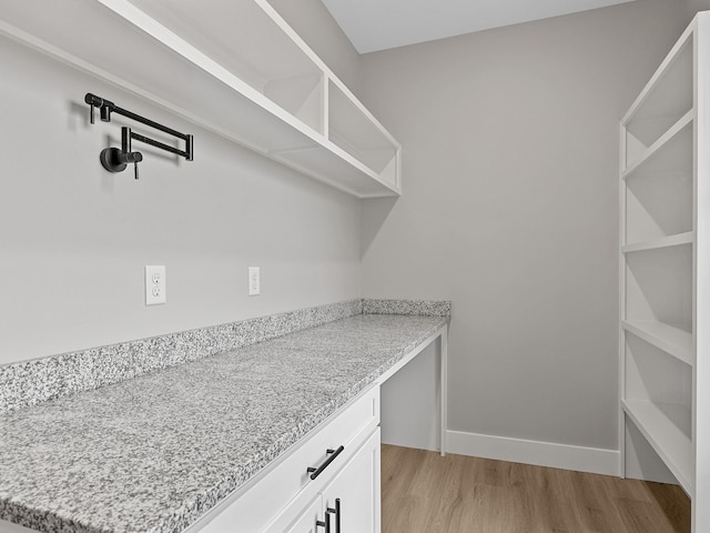 interior space with white cabinets, light hardwood / wood-style floors, and light stone counters