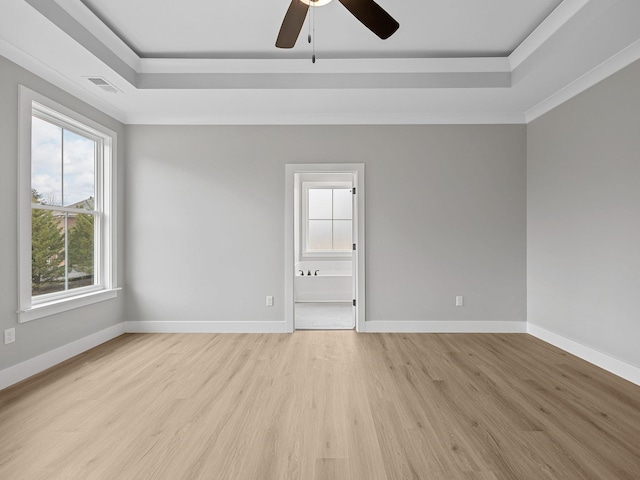 empty room with a raised ceiling, light hardwood / wood-style flooring, ceiling fan, and ornamental molding