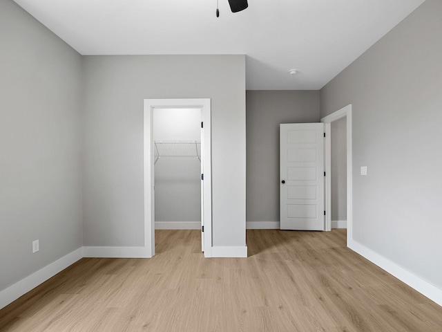 unfurnished bedroom featuring a closet, a walk in closet, light hardwood / wood-style floors, and ceiling fan