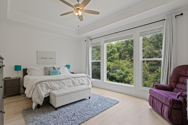 bedroom with light hardwood / wood-style floors, ceiling fan, crown molding, and a tray ceiling