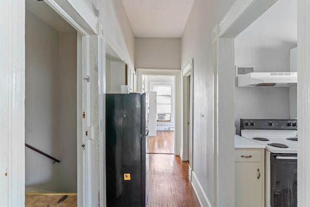 kitchen featuring ventilation hood, white electric range oven, black fridge, and hardwood / wood-style floors