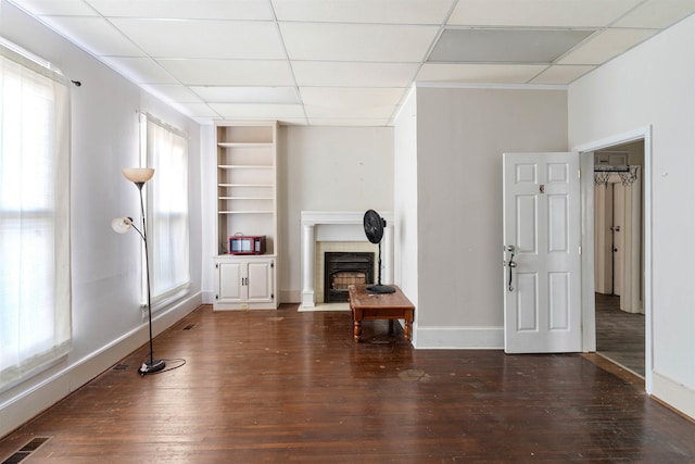 living room with a paneled ceiling, built in shelves, and dark wood-type flooring