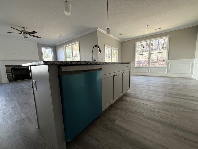 kitchen with hanging light fixtures, ornamental molding, dark hardwood / wood-style floors, dishwashing machine, and an island with sink