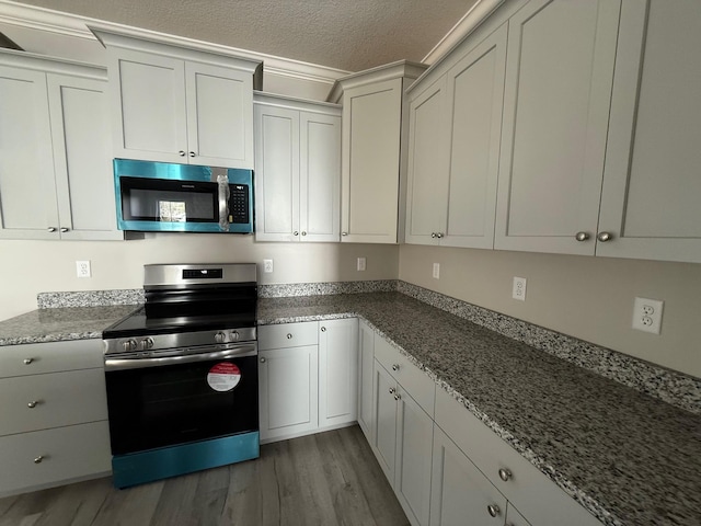 kitchen with hardwood / wood-style flooring, white cabinetry, light stone countertops, a textured ceiling, and stainless steel electric stove