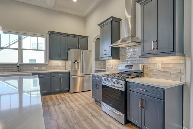 kitchen featuring wall chimney exhaust hood, gray cabinets, decorative backsplash, appliances with stainless steel finishes, and light hardwood / wood-style floors