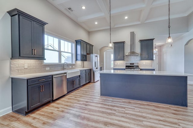 kitchen featuring a center island, wall chimney range hood, light hardwood / wood-style floors, pendant lighting, and appliances with stainless steel finishes