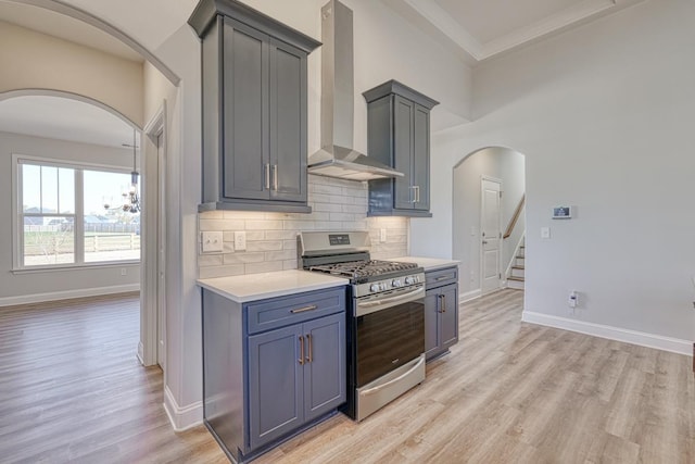 kitchen with wall chimney exhaust hood, tasteful backsplash, light hardwood / wood-style flooring, and gas range