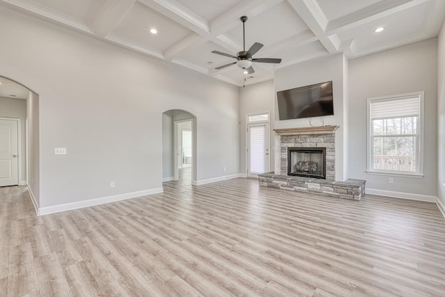 unfurnished living room with ceiling fan, coffered ceiling, a stone fireplace, beamed ceiling, and light wood-type flooring