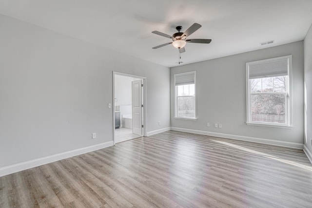 unfurnished bedroom featuring connected bathroom, light hardwood / wood-style floors, multiple windows, and ceiling fan