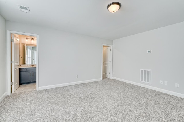 unfurnished bedroom featuring light carpet, ensuite bathroom, and sink