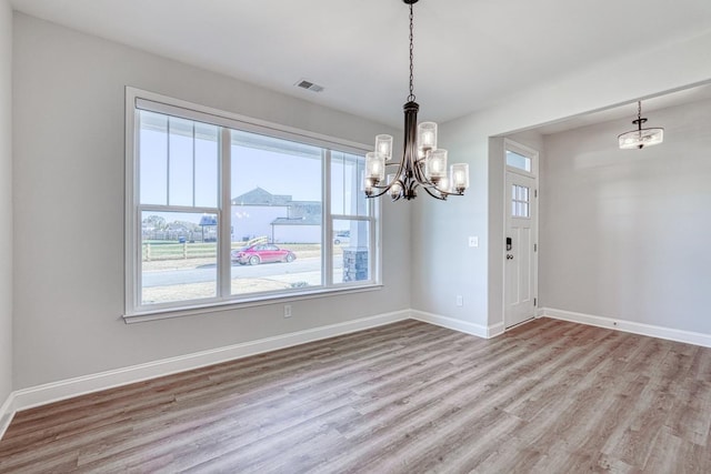 unfurnished dining area with a wealth of natural light, a notable chandelier, and light wood-type flooring