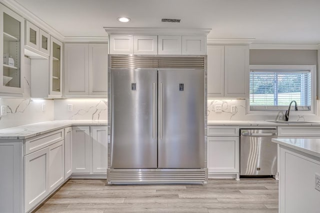 kitchen with decorative backsplash, appliances with stainless steel finishes, sink, white cabinets, and light hardwood / wood-style floors