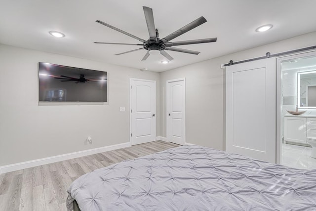 unfurnished bedroom featuring connected bathroom, a barn door, ceiling fan, and light wood-type flooring