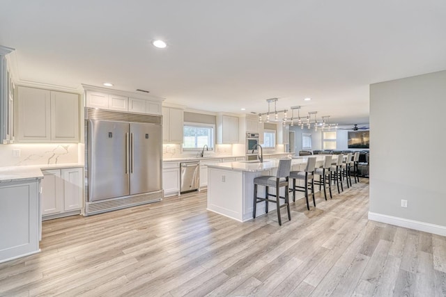 kitchen featuring hanging light fixtures, light hardwood / wood-style floors, stainless steel appliances, and a kitchen island with sink