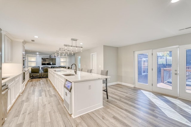 kitchen with light hardwood / wood-style floors, white cabinetry, an island with sink, and hanging light fixtures