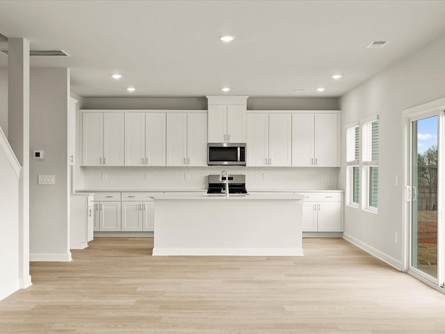 kitchen featuring a kitchen island with sink, light hardwood / wood-style flooring, decorative backsplash, white cabinets, and appliances with stainless steel finishes