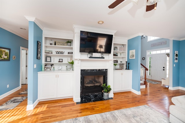 living room with a premium fireplace, light hardwood / wood-style flooring, ceiling fan, and ornamental molding