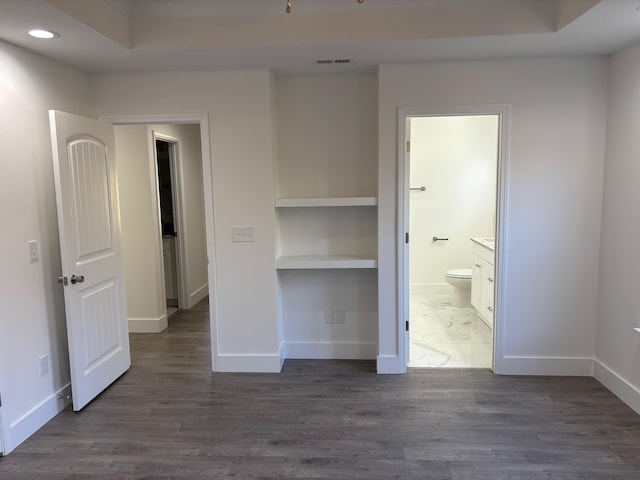 unfurnished bedroom featuring ensuite bathroom, dark hardwood / wood-style flooring, and a tray ceiling