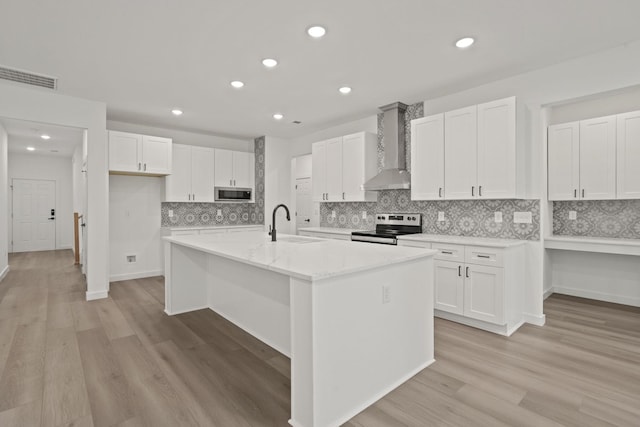 kitchen featuring white cabinets, an island with sink, wall chimney range hood, and appliances with stainless steel finishes