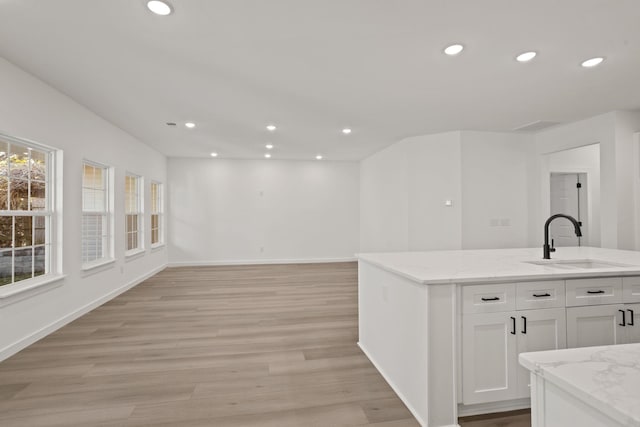 interior space with light stone countertops, light wood-type flooring, white cabinetry, and sink