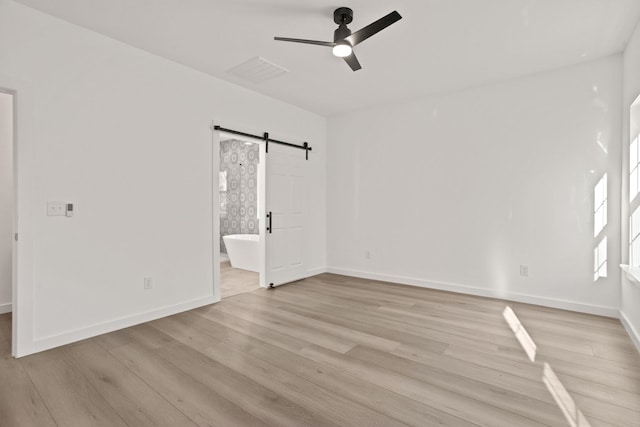 unfurnished bedroom with connected bathroom, a barn door, ceiling fan, and light hardwood / wood-style flooring