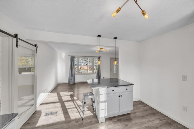 kitchen with dark wood-type flooring, white cabinetry, dark stone countertops, pendant lighting, and a barn door