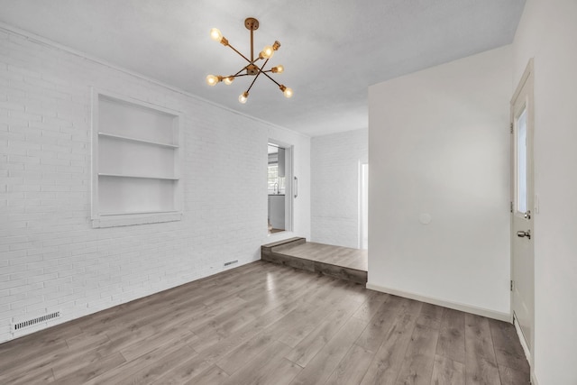 interior space featuring a notable chandelier, hardwood / wood-style flooring, built in features, and brick wall