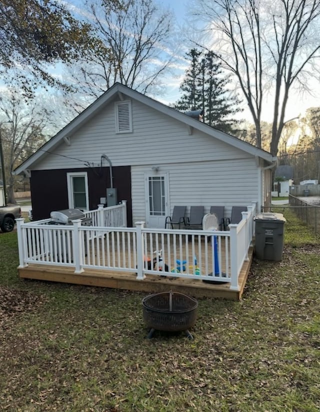 back house at dusk featuring a wooden deck and a fire pit