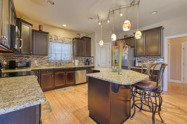 kitchen featuring pendant lighting, light hardwood / wood-style floors, appliances with stainless steel finishes, a kitchen island, and dark brown cabinetry