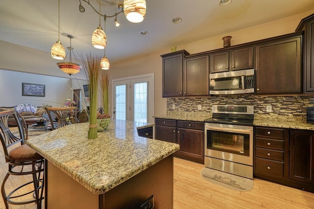 kitchen with a center island, stainless steel appliances, light stone counters, light hardwood / wood-style floors, and decorative light fixtures