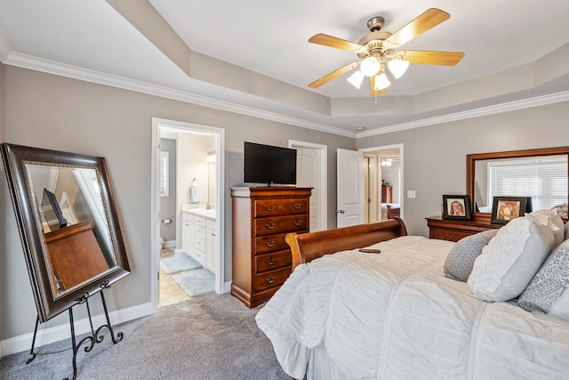 carpeted bedroom featuring a raised ceiling, ensuite bath, and ceiling fan