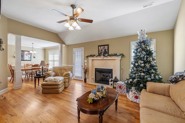 living room featuring ceiling fan with notable chandelier, lofted ceiling, a high end fireplace, and light hardwood / wood-style flooring