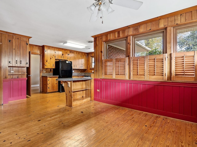 kitchen with black fridge, light hardwood / wood-style flooring, ceiling fan, and wooden walls