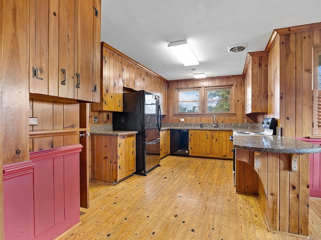 kitchen with sink, light hardwood / wood-style flooring, wooden walls, and black appliances