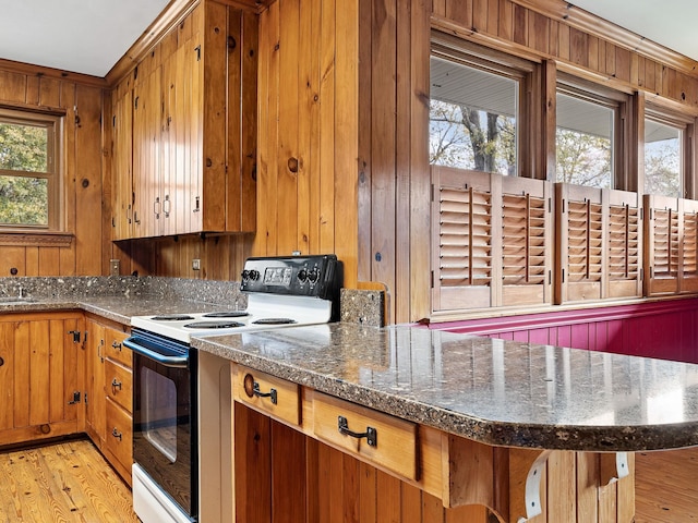 kitchen with white electric range oven, light wood-type flooring, wooden walls, and a healthy amount of sunlight