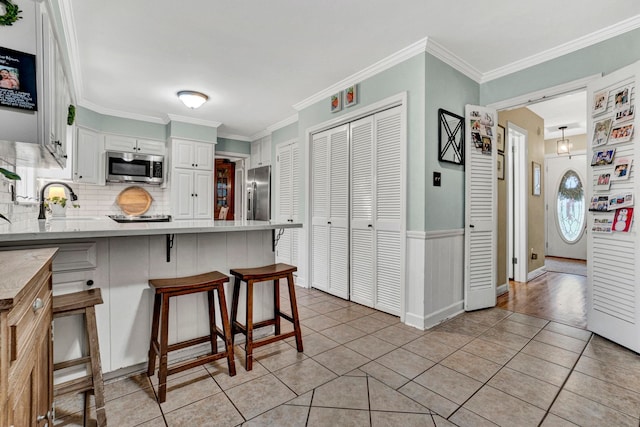 kitchen featuring backsplash, a breakfast bar, stainless steel appliances, crown molding, and white cabinets