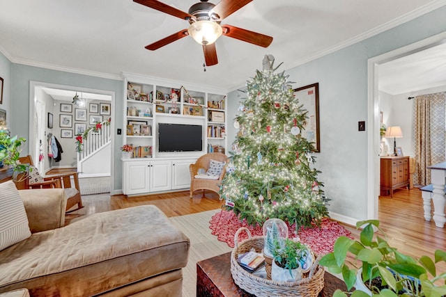 living room featuring ceiling fan, built in shelves, crown molding, and light hardwood / wood-style flooring