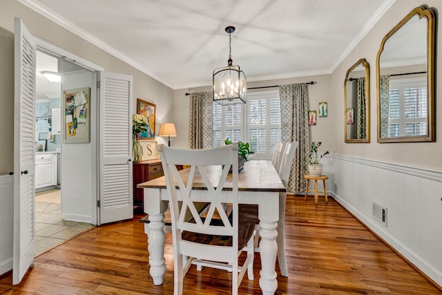 dining area featuring a textured ceiling, light hardwood / wood-style floors, an inviting chandelier, and crown molding