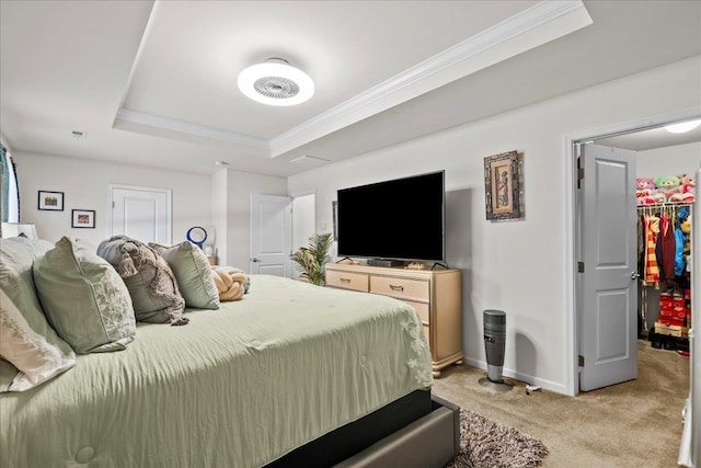 bedroom featuring a raised ceiling, light colored carpet, a walk in closet, and ornamental molding