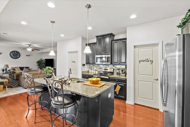 kitchen featuring sink, light hardwood / wood-style flooring, a kitchen island with sink, a breakfast bar, and appliances with stainless steel finishes