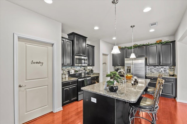 kitchen with a breakfast bar, light wood-type flooring, stainless steel appliances, and a kitchen island with sink