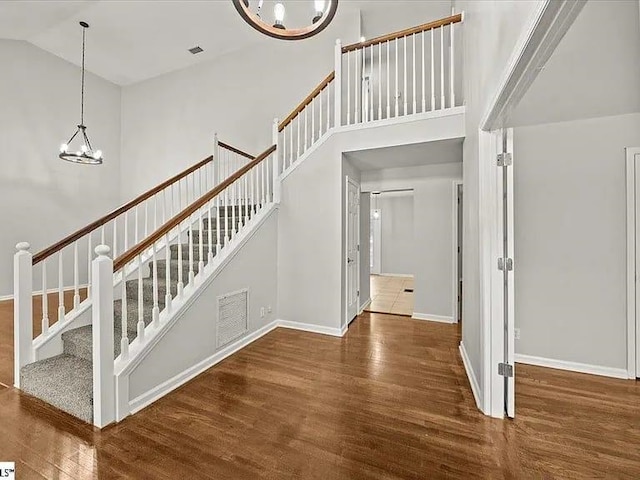 stairway with wood-type flooring, high vaulted ceiling, and an inviting chandelier