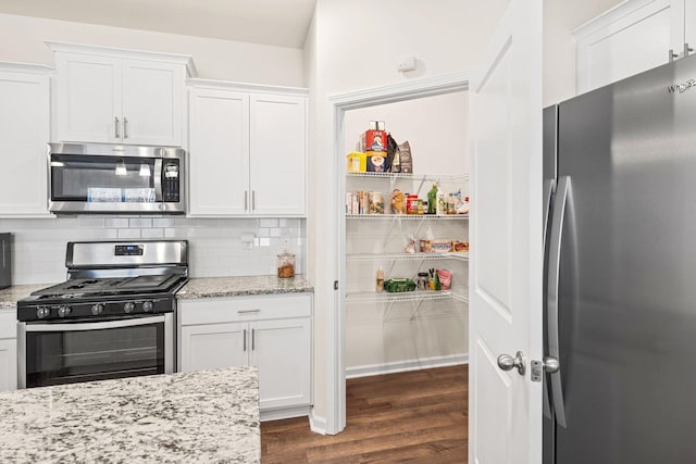 kitchen with backsplash, light stone counters, stainless steel appliances, white cabinets, and dark hardwood / wood-style floors