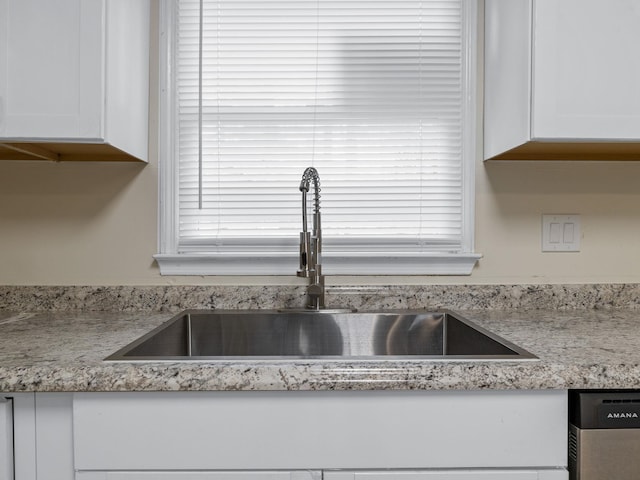 interior details featuring stainless steel dishwasher, light stone countertops, white cabinetry, and sink