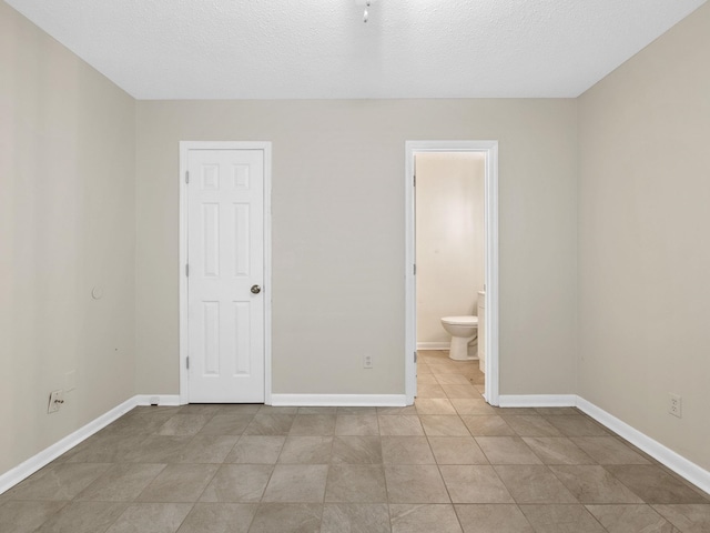 unfurnished bedroom featuring ensuite bathroom, light tile patterned floors, and a textured ceiling