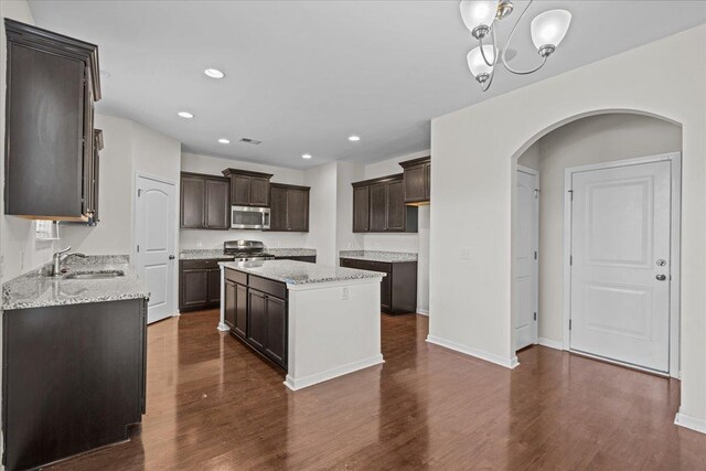 kitchen with appliances with stainless steel finishes, dark hardwood / wood-style flooring, dark brown cabinetry, sink, and a center island