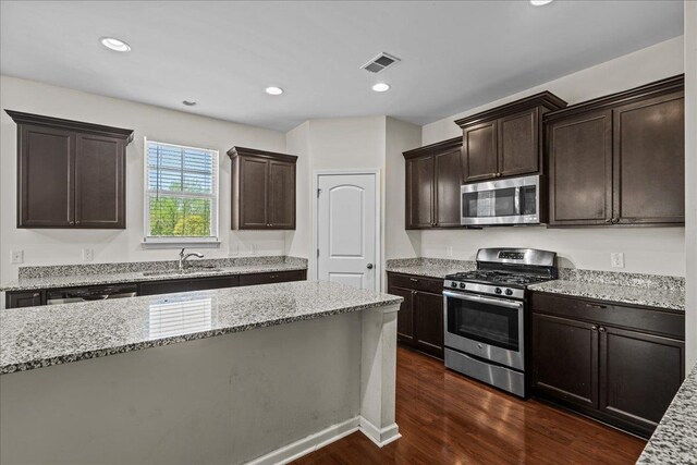 kitchen with light stone counters, sink, dark wood-type flooring, and appliances with stainless steel finishes