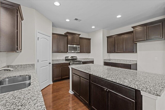 kitchen featuring dark wood-type flooring, sink, appliances with stainless steel finishes, light stone counters, and dark brown cabinetry