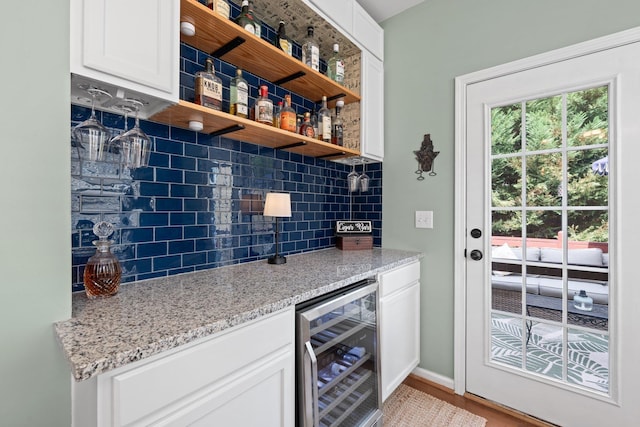 bar with backsplash, white cabinets, wine cooler, light stone countertops, and light hardwood / wood-style floors