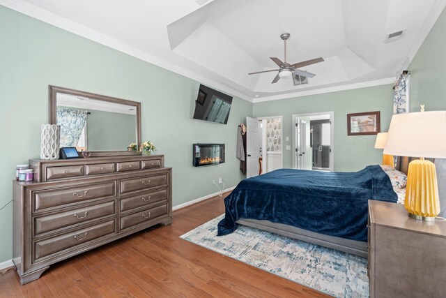 bedroom with ensuite bathroom, ornamental molding, a raised ceiling, ceiling fan, and hardwood / wood-style floors